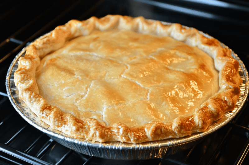 A freshly baked chicken pot pie with a golden crust, creamy filling, and colorful vegetables on a rustic wooden table